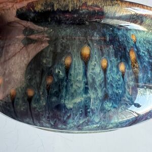 This pottery bowl features a complex glaze with drips of blue, purple, and bronz